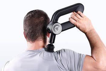 Person using a handheld massage gun on their neck, showcasing the device's ergonomic handle and round massaging head