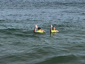 Two people with neon yellow buoys floating and waving in the sea