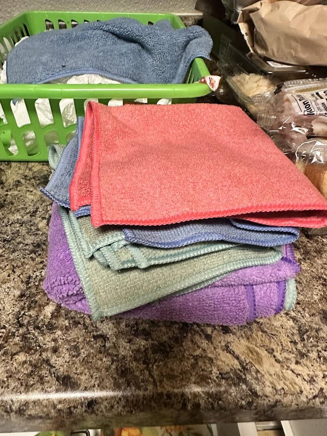 Stack of folded cleaning cloths on a countertop, next to a green basket holding more cloths