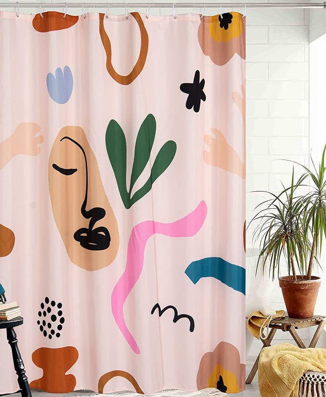 the pale pink shower curtain printed with colorful flowers, squiggles, and an abstract face