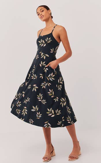 a model wearing the sleeveless midi dress in black with a tan leaf print 