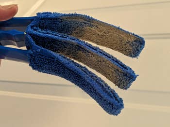 Reviewer holding the three-prong blue blinds duster covered in dust