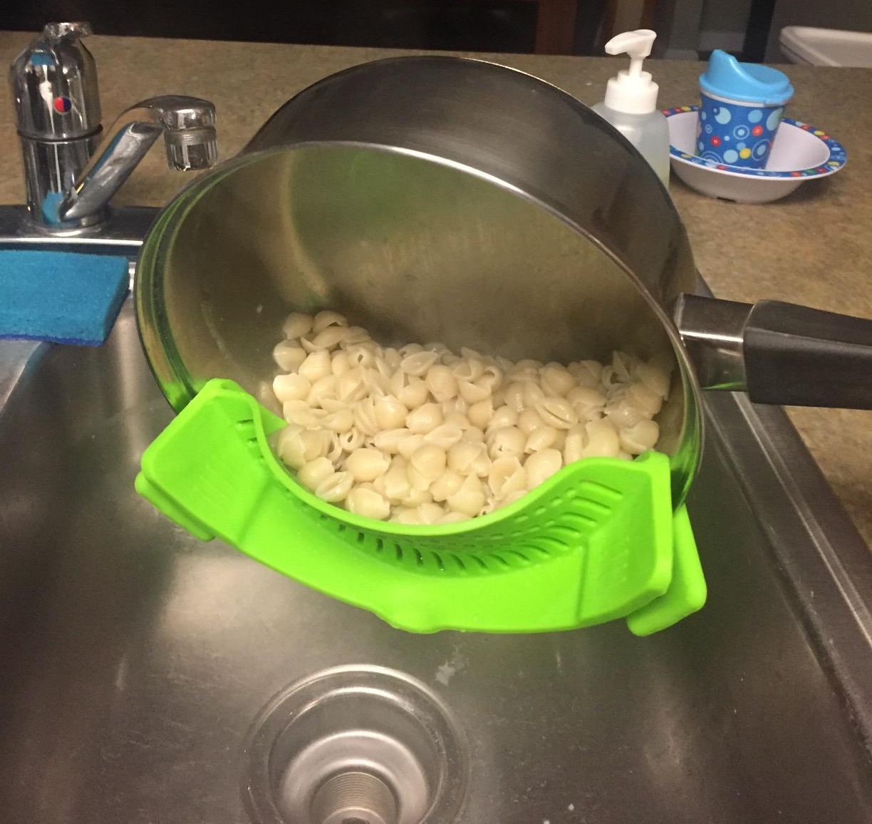 reviewer photo of the green strainer attached to the side of a pot, showing all the water has been strained out but the macaroni shells are still in the pot