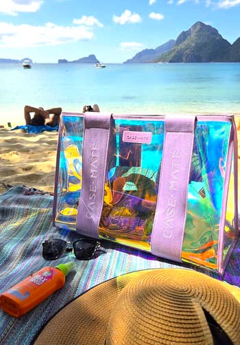 Clear formation  container  with pinkish  straps connected  a sandy beach, adjacent   sunglasses, sunblock, and a straw hat, with radical   lounging by the sea