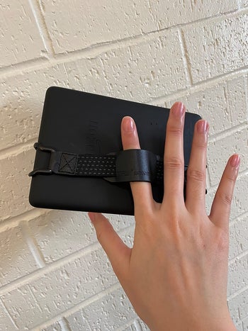 reviewer showing the strap attached to the back of a Kindle and how one finger fits in it