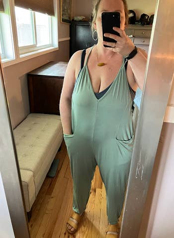 reviewer taking mirror selfie while wearing the sage color jumpsuit