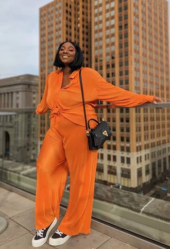 reviewer in a stylish orange jumpsuit with a shoulder bag, posing confidently in an urban setting