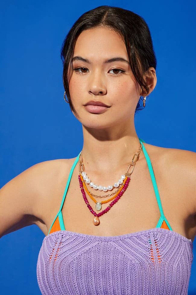 model wearing the four layer gold orange magenta and white necklace with a bathing suit and coverup