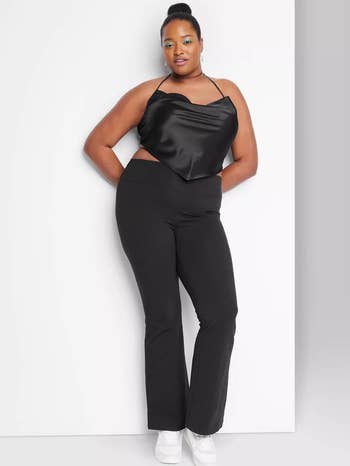 Woman in black one-shoulder top and pants poses, suitable for plus-size fashion shoppers