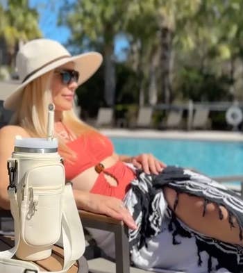 model lounging by a pool with a water bottle strapped into a fitted bag on table next to them