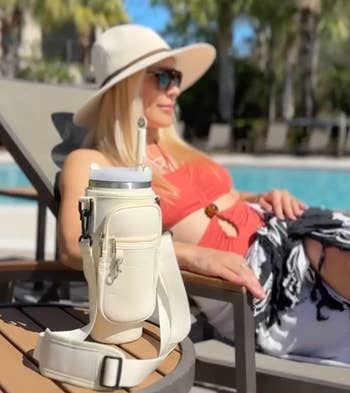 Model bersantai di dekat kolam dengan botol air yang diikat ke dalam tas yang pas di atas meja di sebelahnya