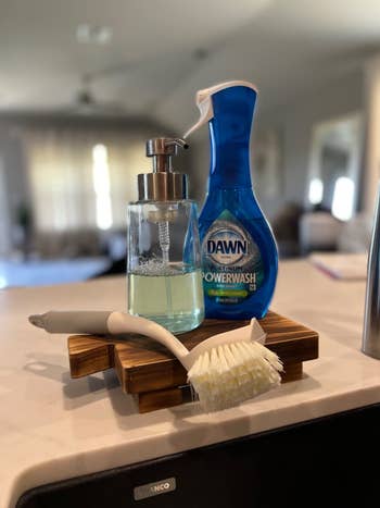 A Dawn Platinum Powerwash dish spray sits next to a soap dispenser and a dish brush on a kitchen counter