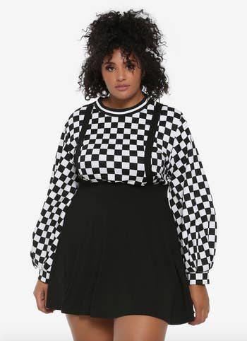 a model wearing a black skirt with suspenders over a checkerboard long sleeve