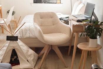 Reviewer image of cream fabric chair with four wooden legs in front of bedroom desk with laptop