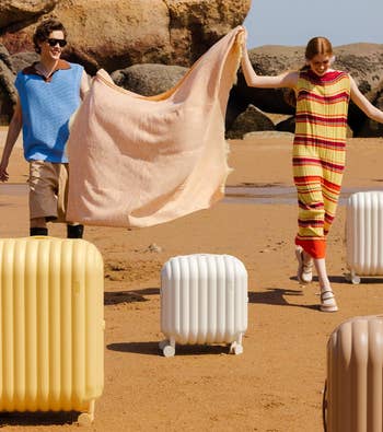 Two models strolling on a beach holding a towel, with trendy luggage by their side, in casual beachwear