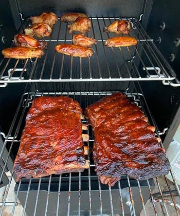 closeup of two racks of ribs and wings cooking inside reviewer's smoker