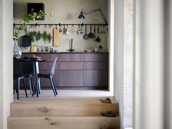Minimalist kitchen with wood cabinets, wall-mounted utensils, and a dining table with chairs in the foreground. Modern and functional design