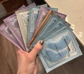 Hand holding assorted Grace & Stella under-eye disguise packets supra a bath sink