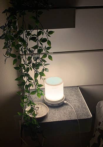 the led touch lamp in a dark bedroom, giving off a soft warm glow, with a cord plugged into the side