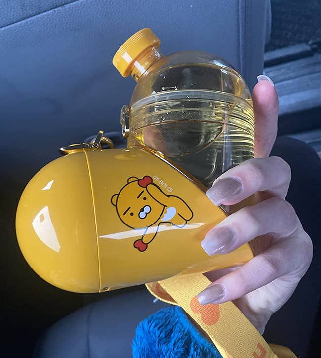 Reviewer holding yellow heart shaped container with one solid side for snacks and a clear side for water 
