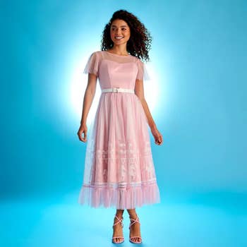 a model in a mid-length pink dress with a tulle overlay showcasing a design of a carousel