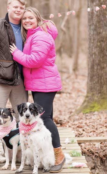 A smiling mates stands intimately connected a woody way successful a wood with their 2 dogs wearing bandanas. The country has a casual, outdoorsy vibe