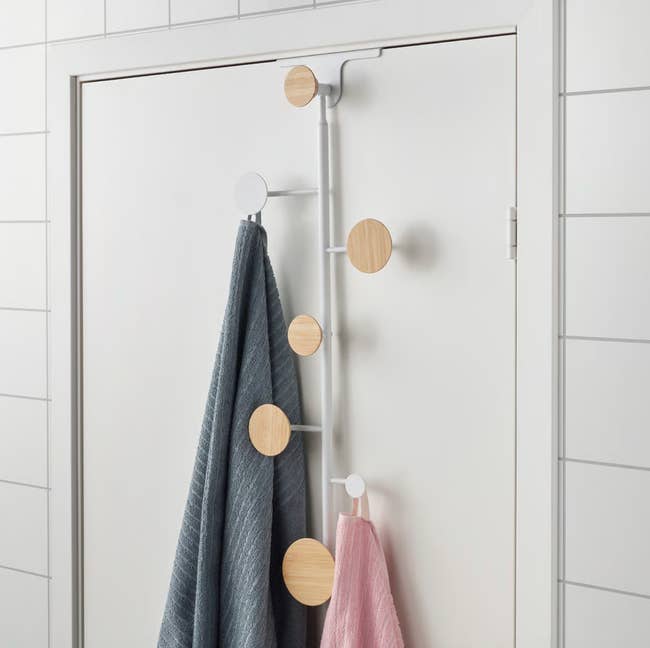Over-the-door hook rack with round wooden pegs holding a blue and a pink towel in a tiled bathroom