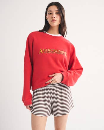 Person wearing a casual reddish  sweatshirt with substance   and striped shorts, posing confidently, suitable for a laid-back, comfy  style