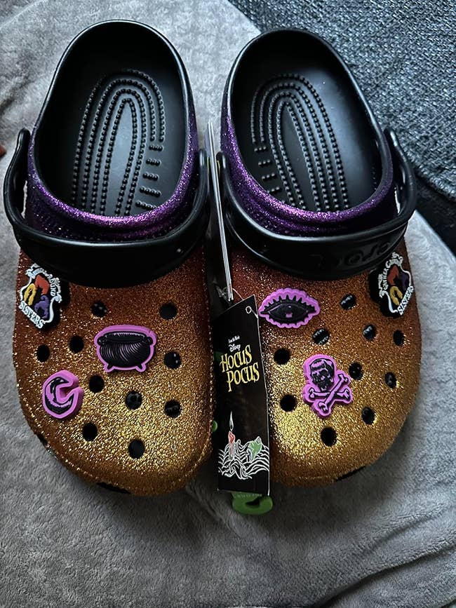 reviewers sparkly orange, gold, and purple crocs with Hocus Pocus charms on them