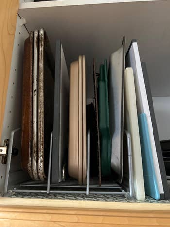 Kitchen cabinet neatly organized with various baking sheets and cutting boards stored vertically in a rack
