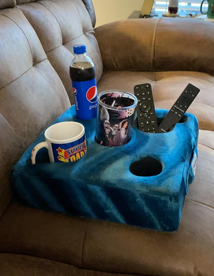 A blue pillow with five holes fitting a can, a drink, a remote control, and a phone 