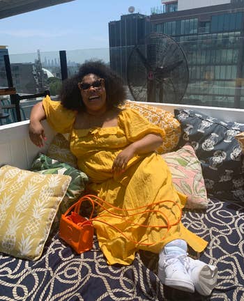 Reviewer in a flowing yellow dress lounges on a patterned sofa outdoors