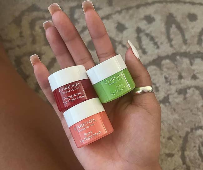 Hand holding two CARE:NEL lip masks: berry, pomegranate, and lime