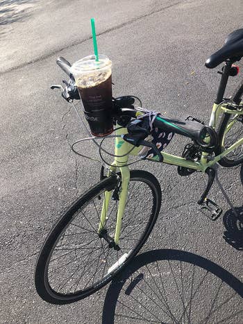 a reviewer photo of the car cupholder mounted on a bike with a plastic iced coffee cup in it 