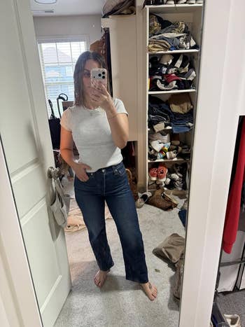 Person successful  reflector  selfie wearing a achromatic  T-shirt and jeans; cluttered closet successful  inheritance  with apparel  and shoes visible