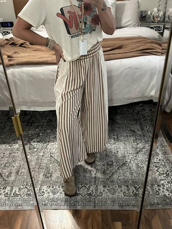 reviewer  in a graphic t-shirt and striped wide-leg pants, reflected in a bedroom mirror, showcasing a casual outfit style