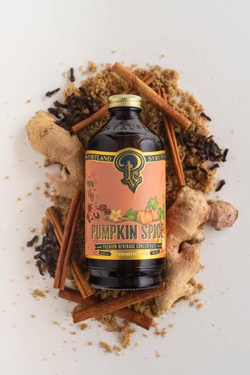 Pumpkin spice syrup vessel  surrounded by ginger, cinnamon sticks, and spices, styled for a buying  article