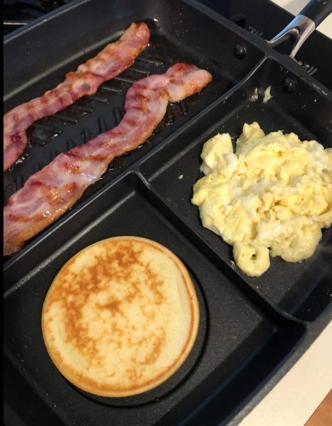 A three-sectioned skillet cooking bacon, a pancake, and eggs 
