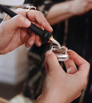 a model dipping the guide wand into a small pot of brown eyeliner 