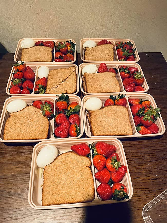 Several of the food containers packed with a sandwich, boiled egg, and strawberries