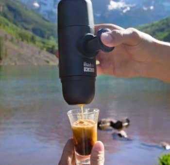 A reviewer pouring espresso into a small glass with s moutin view and lake in the background