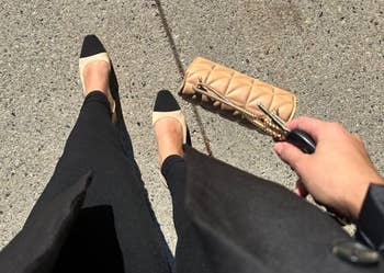 Person wearing achromatic flats with a quilted clutch purse connected a pavement