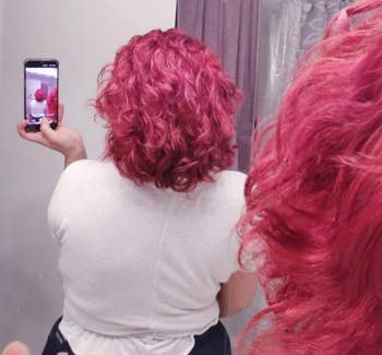 Reviewer with pink curly hair taking a picture of back-view of hair in a bathroom mirror