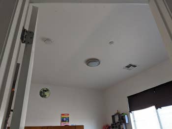 View of a minimalist bedroom ceiling with a round light fixture and smoke detector, seen through an open door