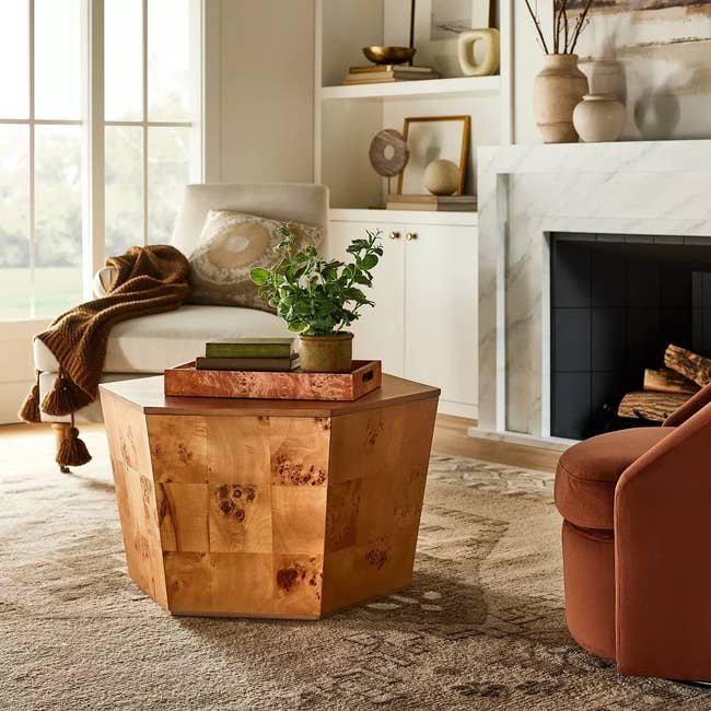 A polished wood side table in a cozy living room setting with a plant on top, near a fireplace and seating