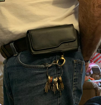 Reviewer wearing black leather phone case horizontally attached to black belt with keys clipped onto it