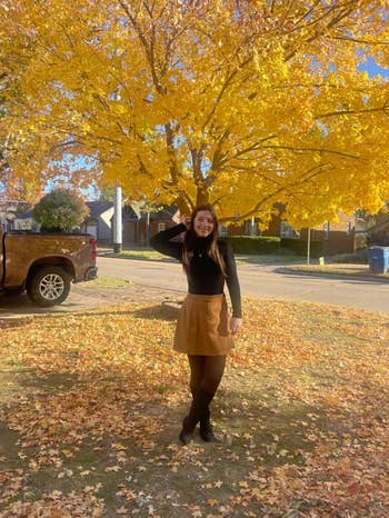 Person successful  a achromatic  apical  and tan skirt poses nether  a aureate  autumn tree, smiling