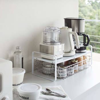 the white expandable organizer on a countertop holding coffee maker and other items