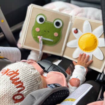 Baby successful  a car   spot   touches a brushed  cloth  publication  with frog and angiosperm  designs, wearing a knit hat