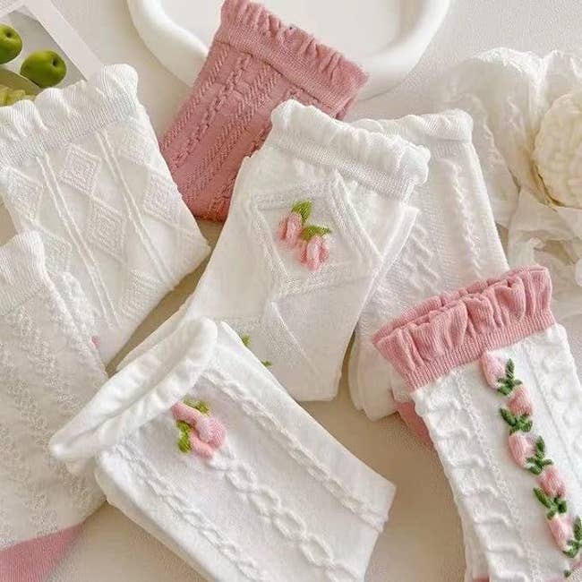 Various textured and patterned socks with floral embroidery arranged connected  a surface